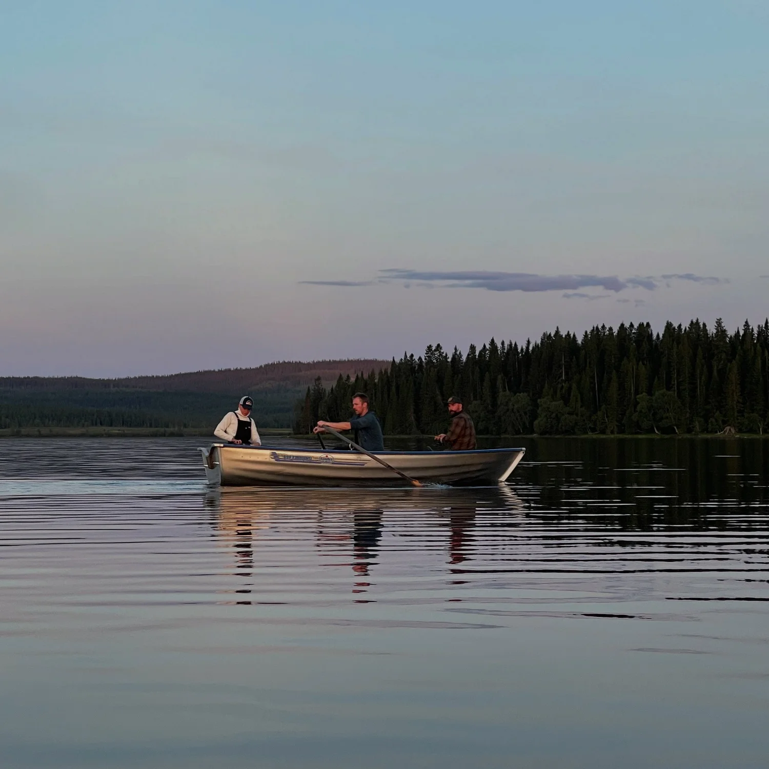 Tre personer fiskar från en eka i skymningen på en fjällsjö